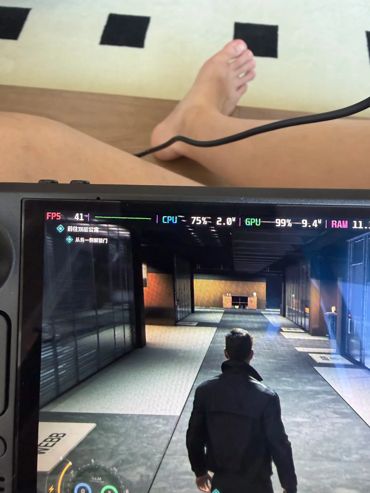 A handheld gaming console displaying a third-person video game with a performance overlay showing 41 FPS, with a person's bare legs resting in the background.