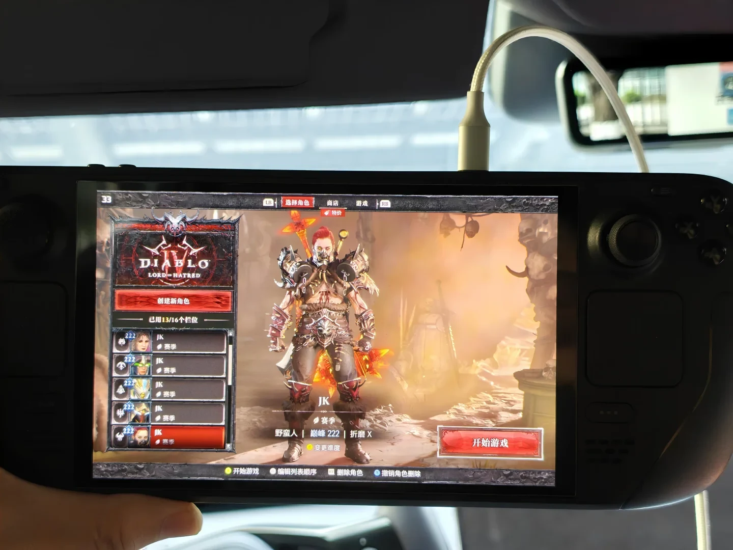 A Steam Deck handheld console running Diablo IV: Vessel of Hatred inside a car, displaying a barbarian on the character selection screen.