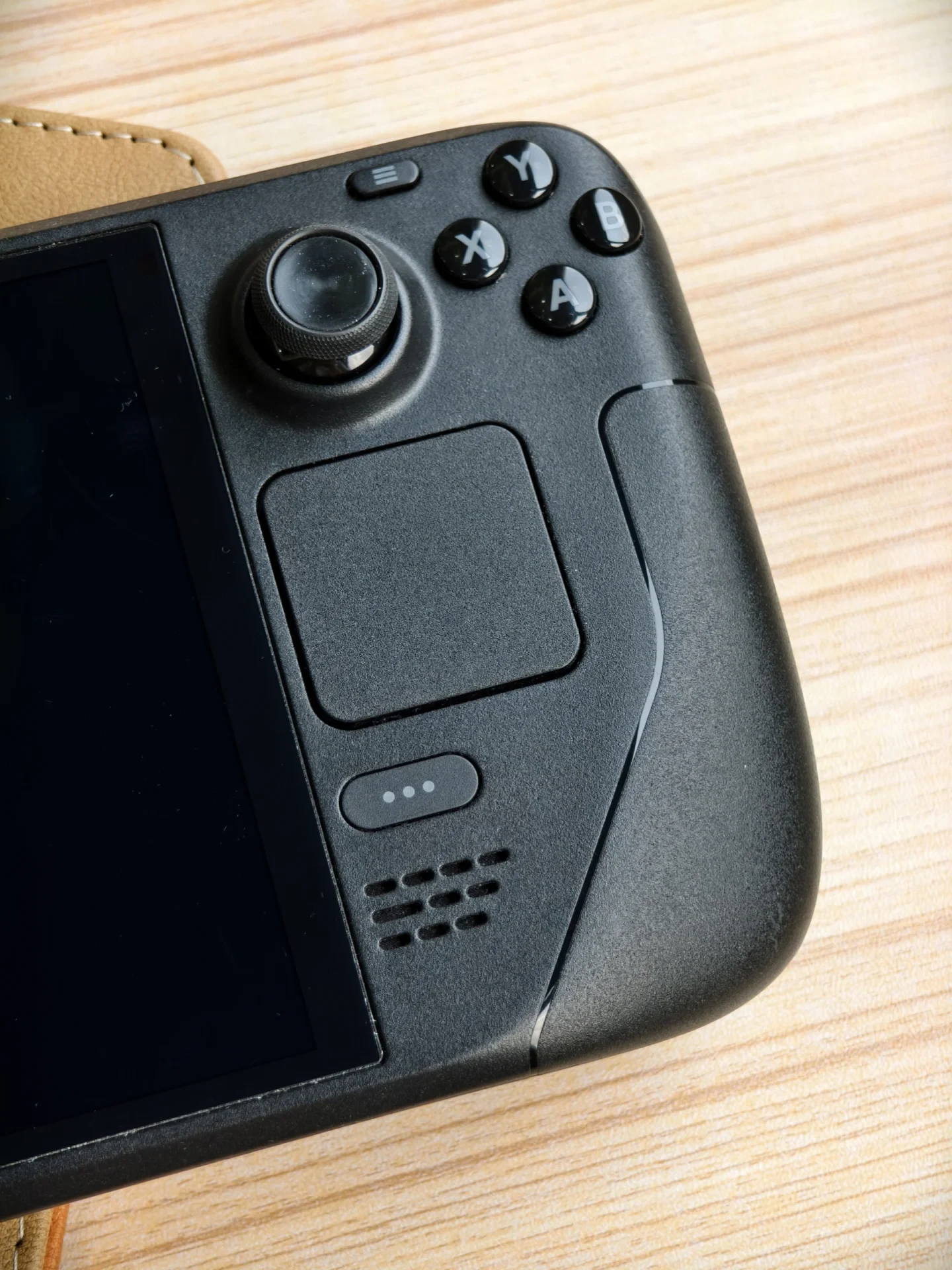 Close-up view of the right control section of a black Valve Steam Deck handheld console on a wooden surface, showing the joystick, ABXY buttons, square trackpad, Quick Access button, and speaker grille.