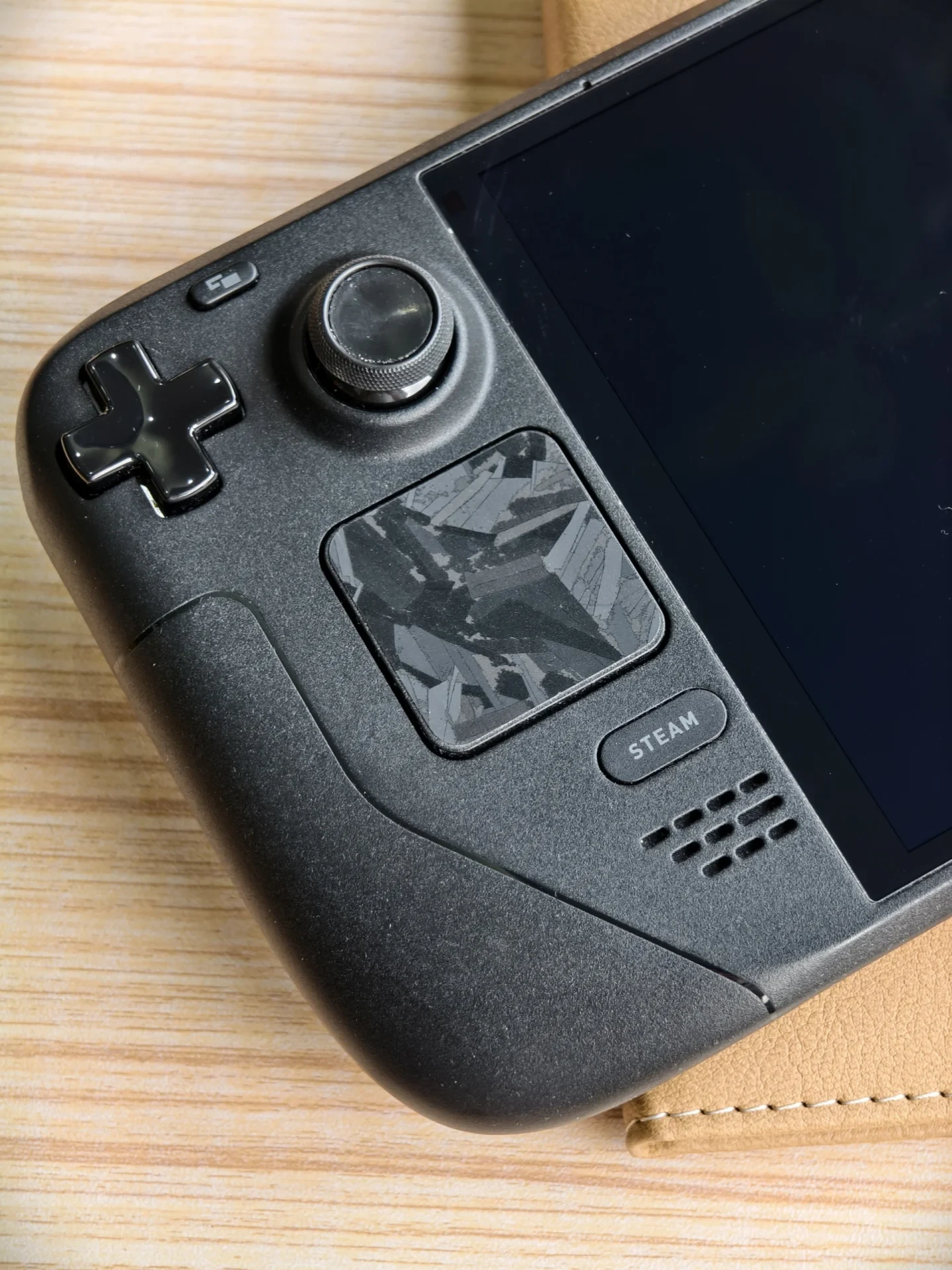 Close-up of the left side of a black Steam Deck handheld gaming console, featuring a geometric patterned skin applied to the square trackpad.