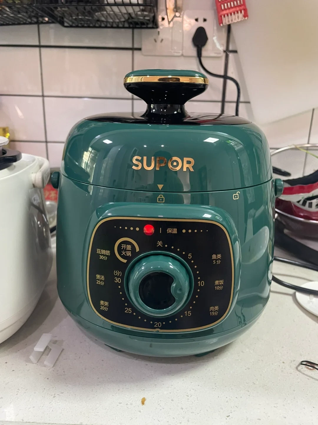 A dark green Supor electric pressure cooker sitting on a kitchen countertop with a rotary dial control panel on the front.