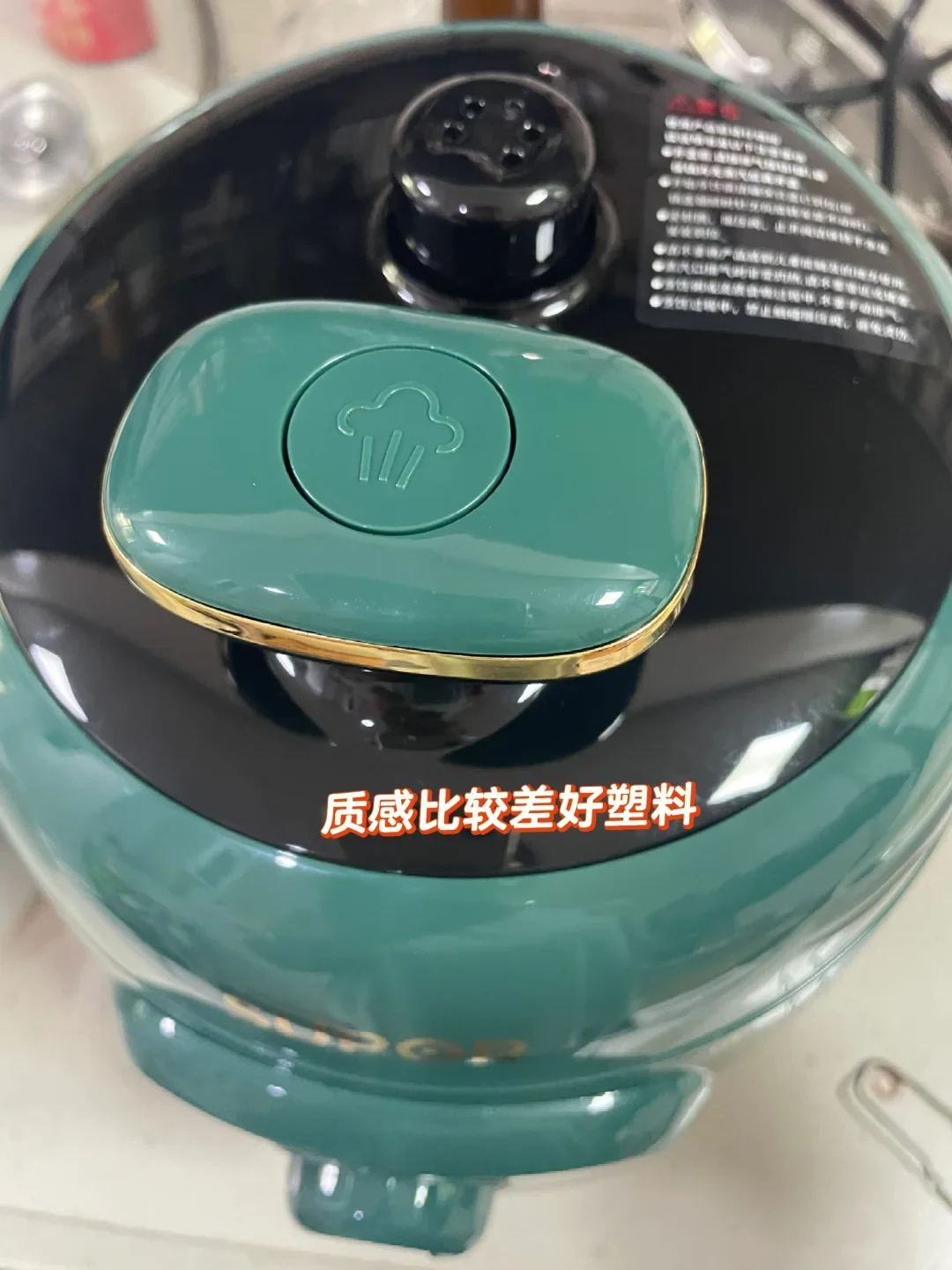 Top-down close-up of a green and black electric pressure cooker lid showing the steam release button and pressure valve, with an overlaid user review comment.