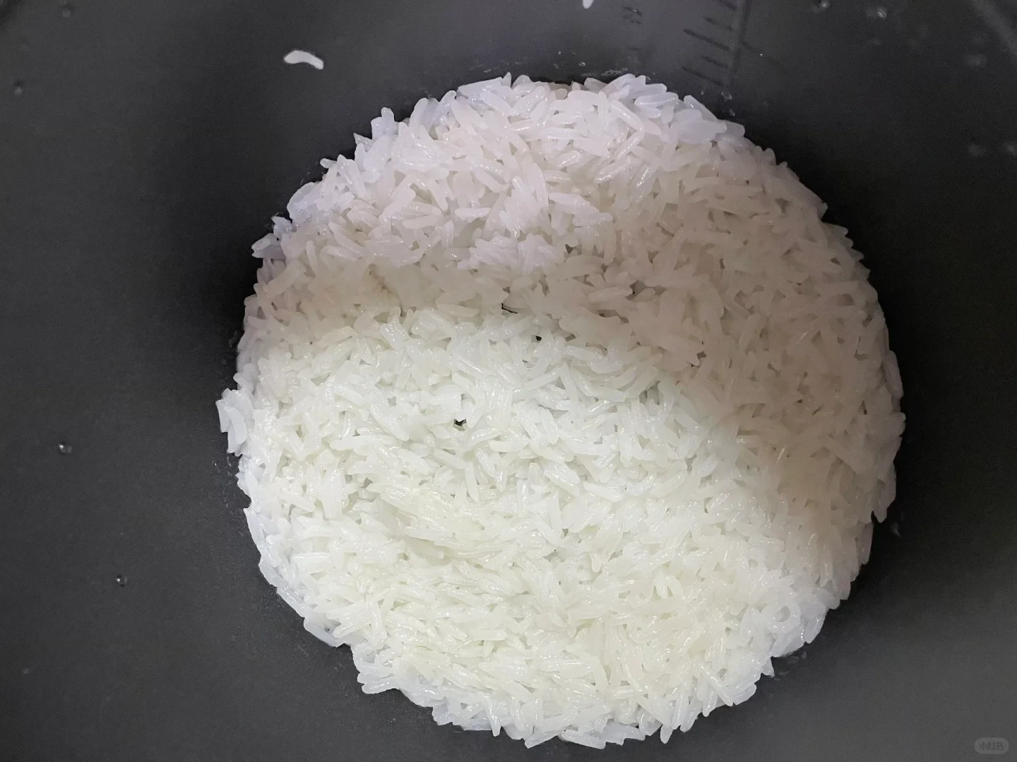 Top-down view of cooked white rice inside the black inner pot of a rice cooker.