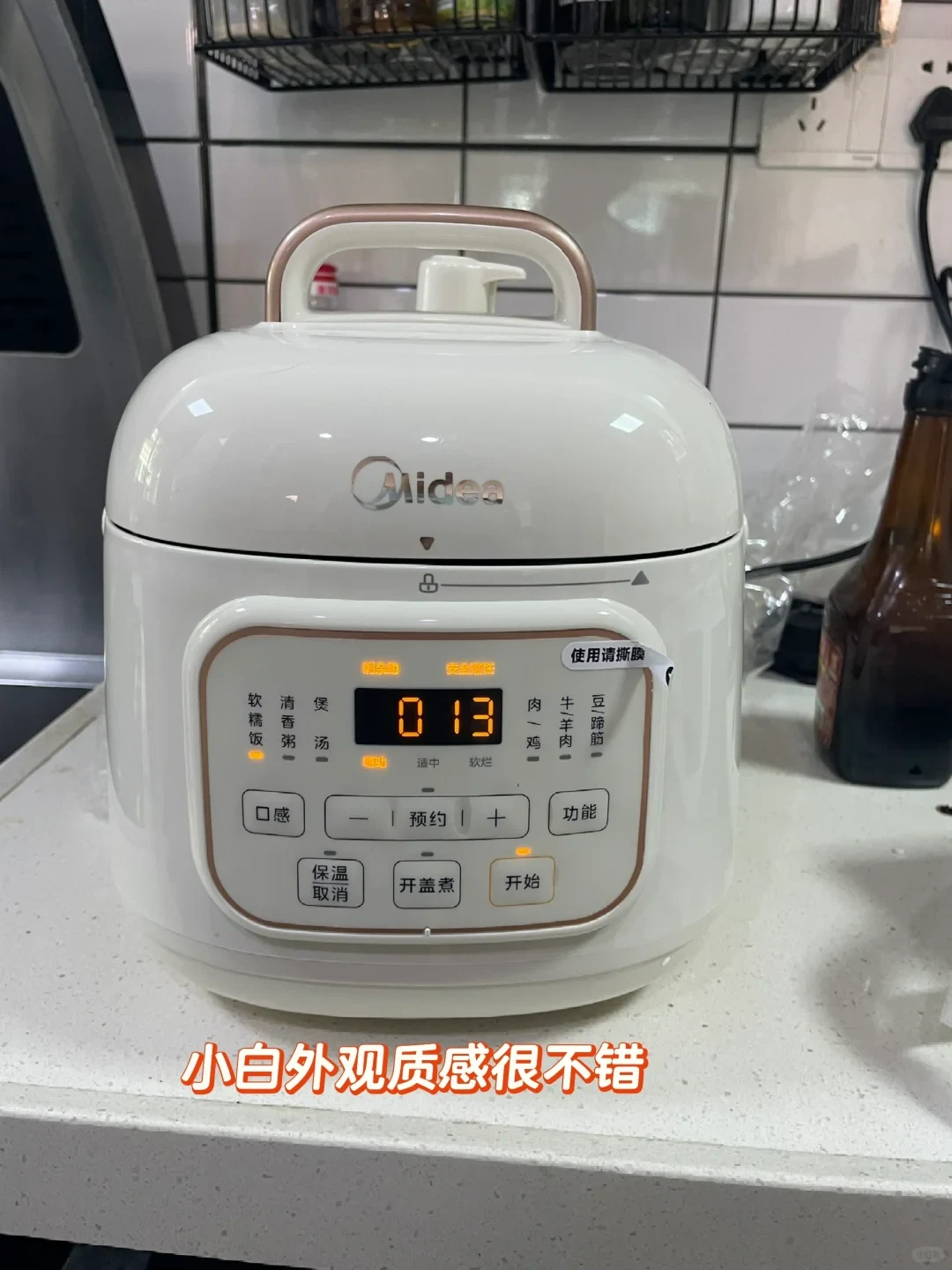A white Midea electric pressure cooker sitting on a kitchen countertop, featuring a digital display reading 013 and Chinese control buttons.