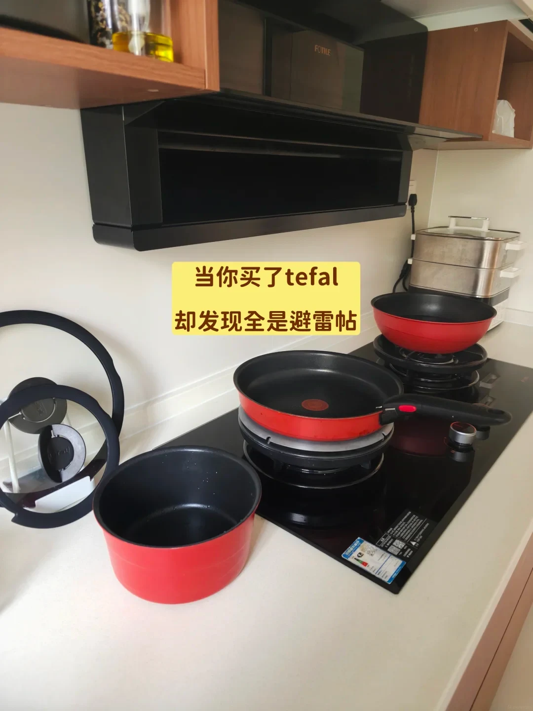 A red Tefal non-stick cookware set with a detachable handle arranged on a black glass cooktop and kitchen counter.