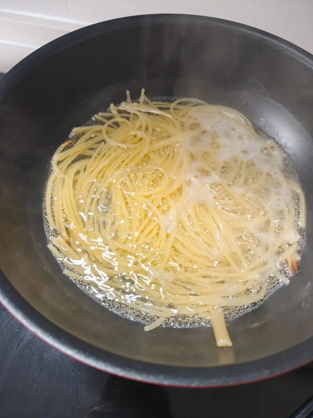 Spaghetti noodles boiling in bubbling water inside a deep black non-stick Tefal pan.