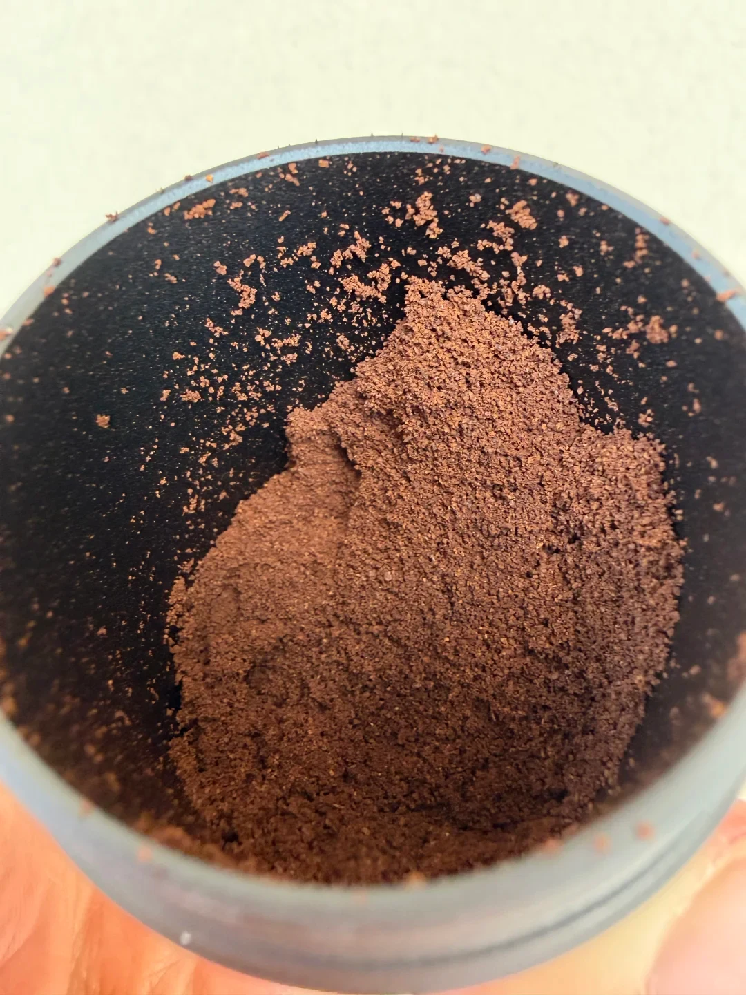 Coffee grounds form a small mound in the grinder’s metal catch cup, with loose grounds around the dark inner wall.