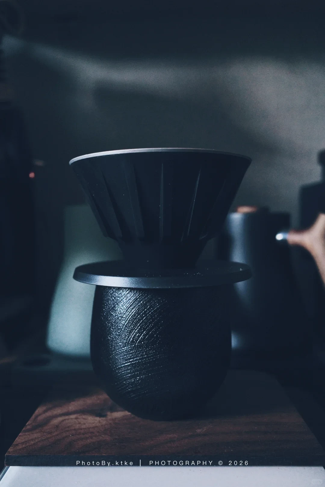 The VECTOR dripper, fitted with its black sleeve and base, sits on a dark textured cup beside a kettle.