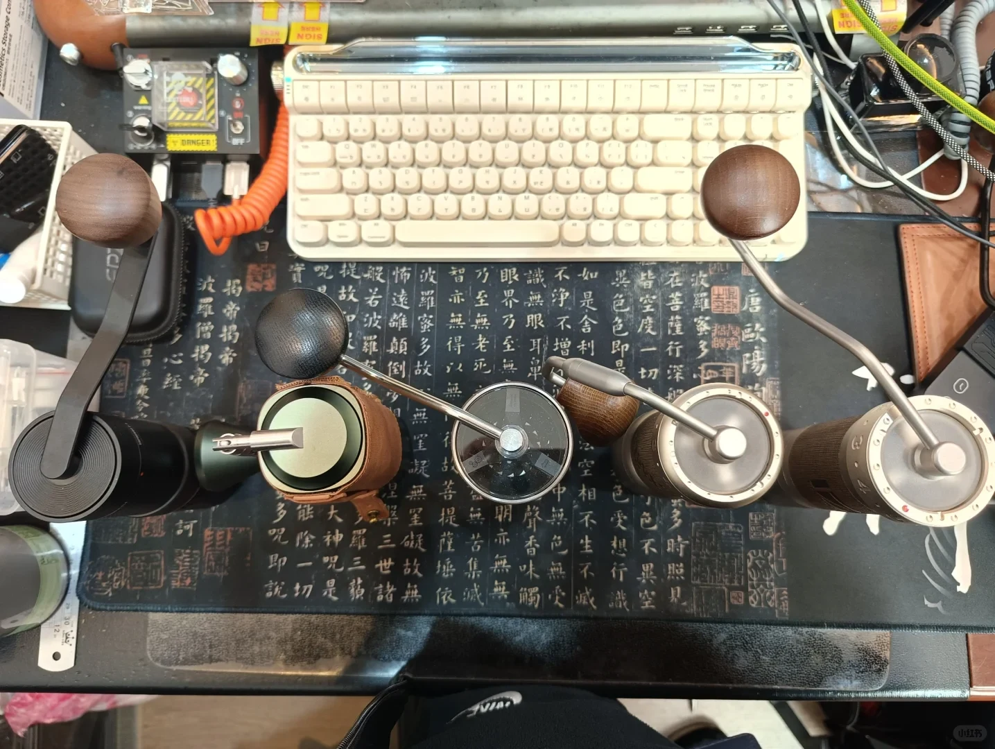 Overhead view of the five manual coffee grinders with their cranks and knobs, arranged on a desk mat beside a keyboard.