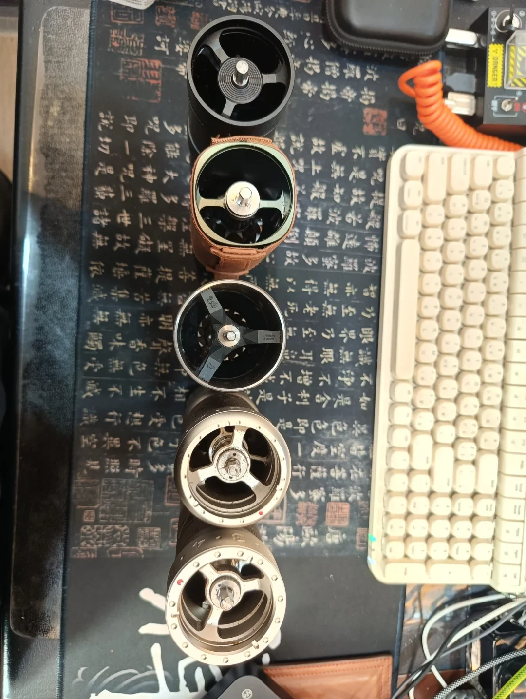 Five manual coffee grinders with their handles and lids removed, showing their open tops and interior supports on a desk mat.