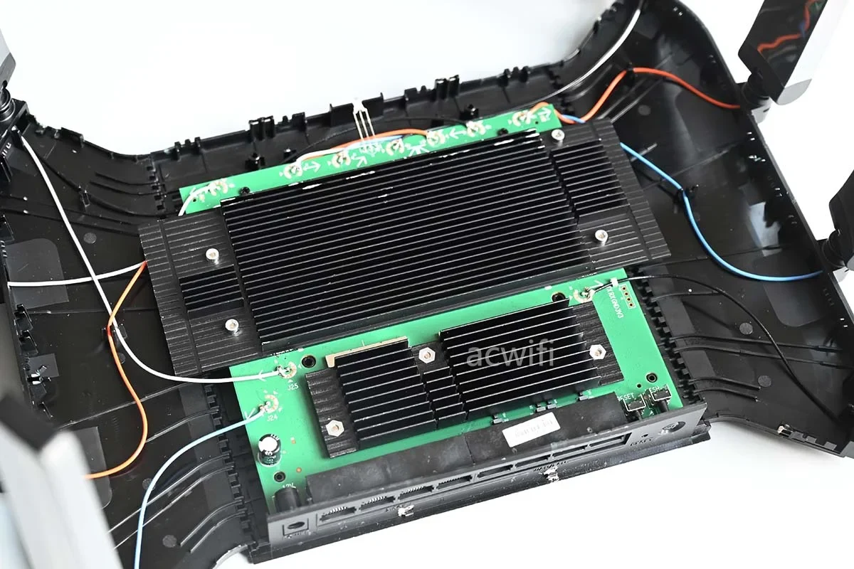 High-angle view inside the opened casing of a disassembled TP-Link router, showing green printed circuit boards fitted with large black finned heatsinks and internal antenna wires routed around the chassis.