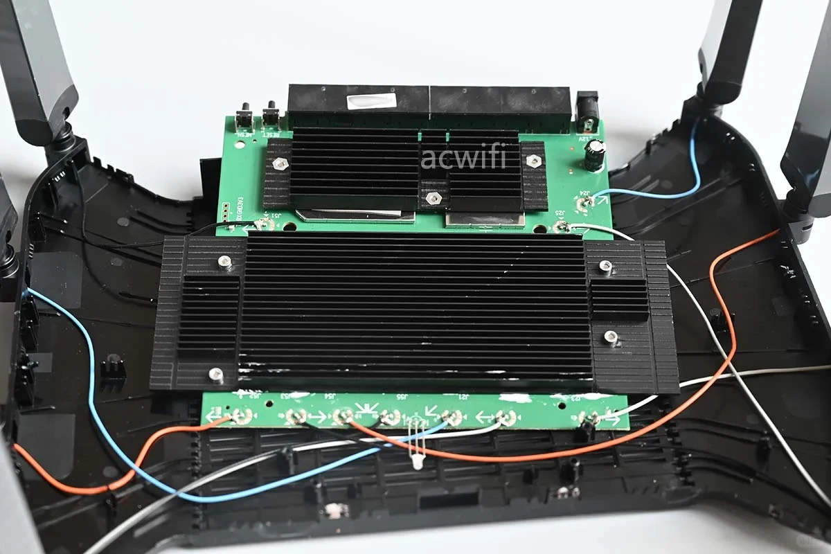 Teardown view of the TP-LINK 7DR7290 router interior showing the green circuit board mounted with two large black finned heatsinks and colored antenna wires inside the opened casing.