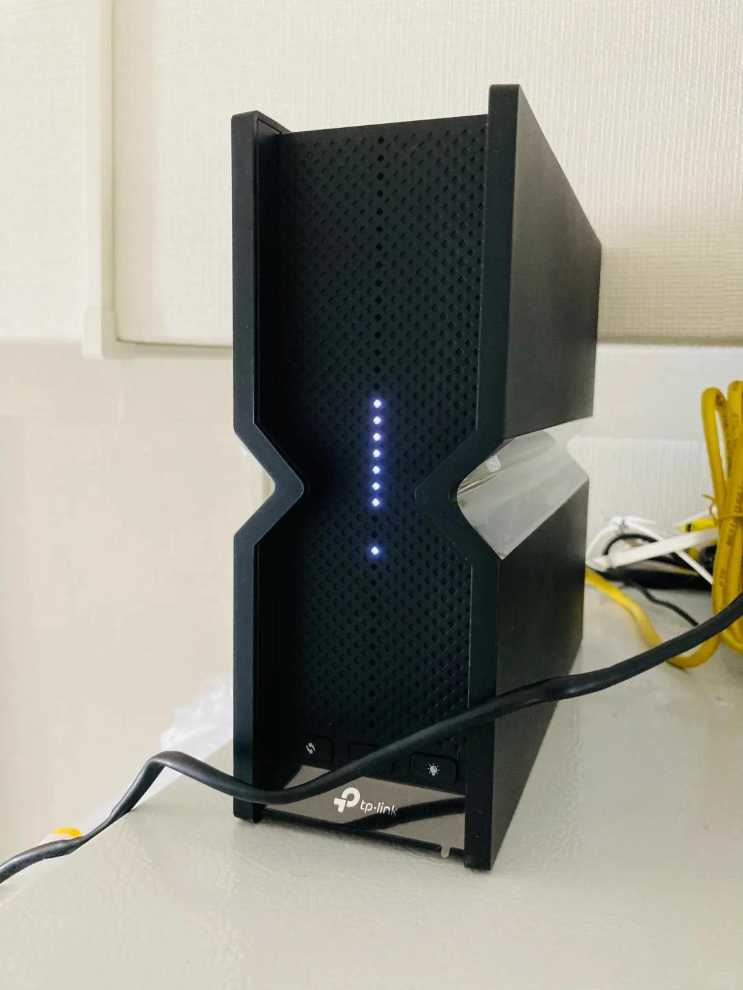 A black upright TP-Link Wi-Fi router standing on a white surface with small vertical status lights illuminated on the front panel.