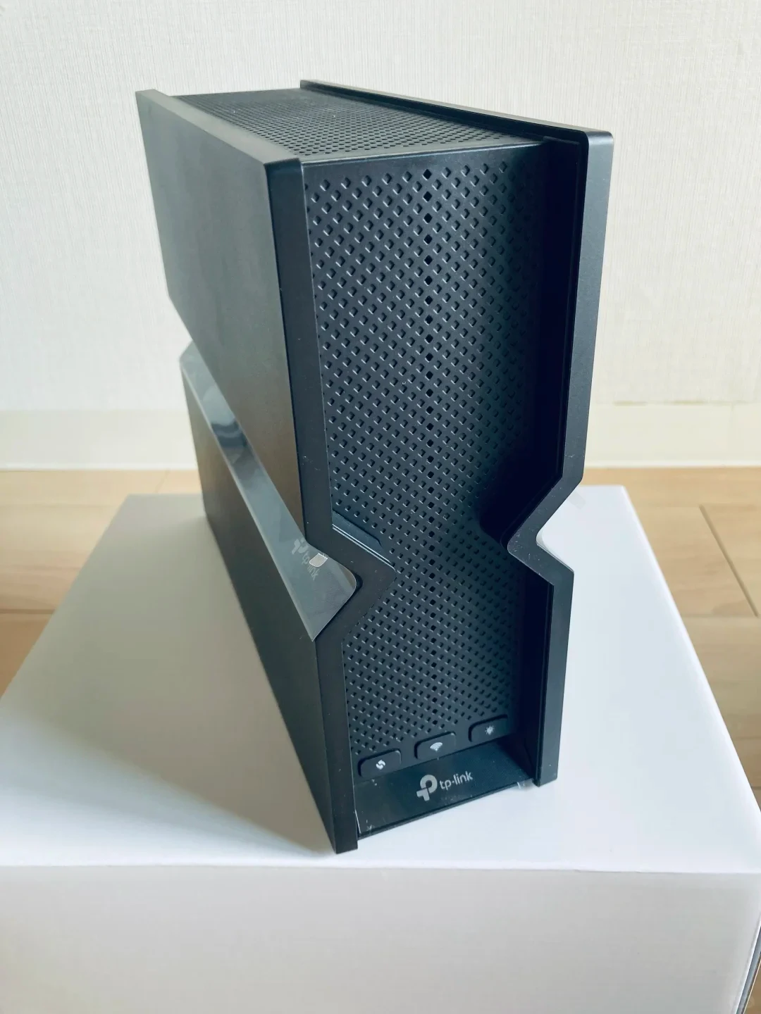A black TP-Link vertical Wi-Fi router with a textured front panel sitting upright on a white box.