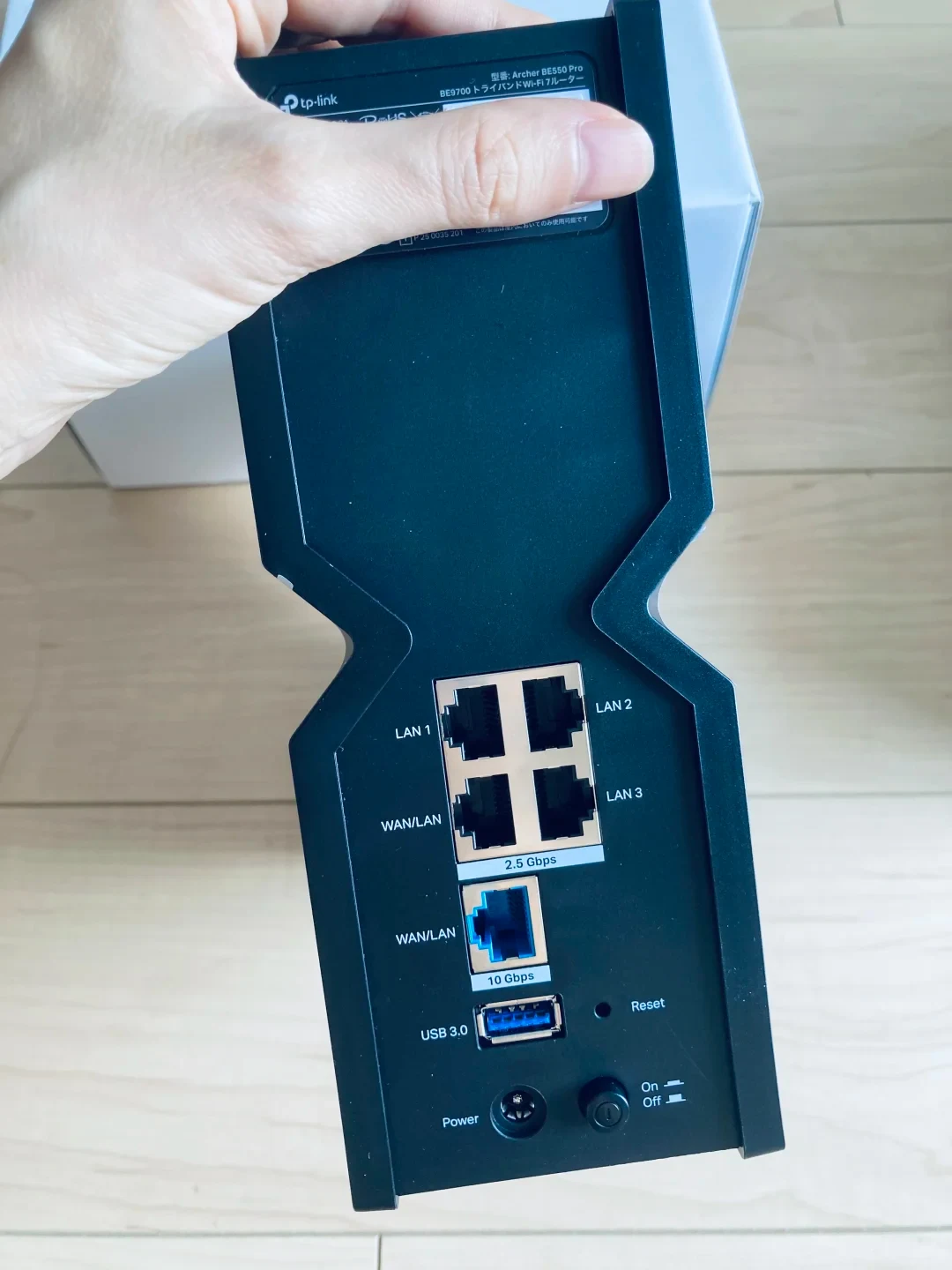 A hand holding the rear side of a black TP-Link Archer BE550 Pro Wi-Fi router, showing four 2.5 Gbps Ethernet ports, one 10 Gbps WAN/LAN port, a USB 3.0 port, a reset pinhole, a power jack, and a power button.