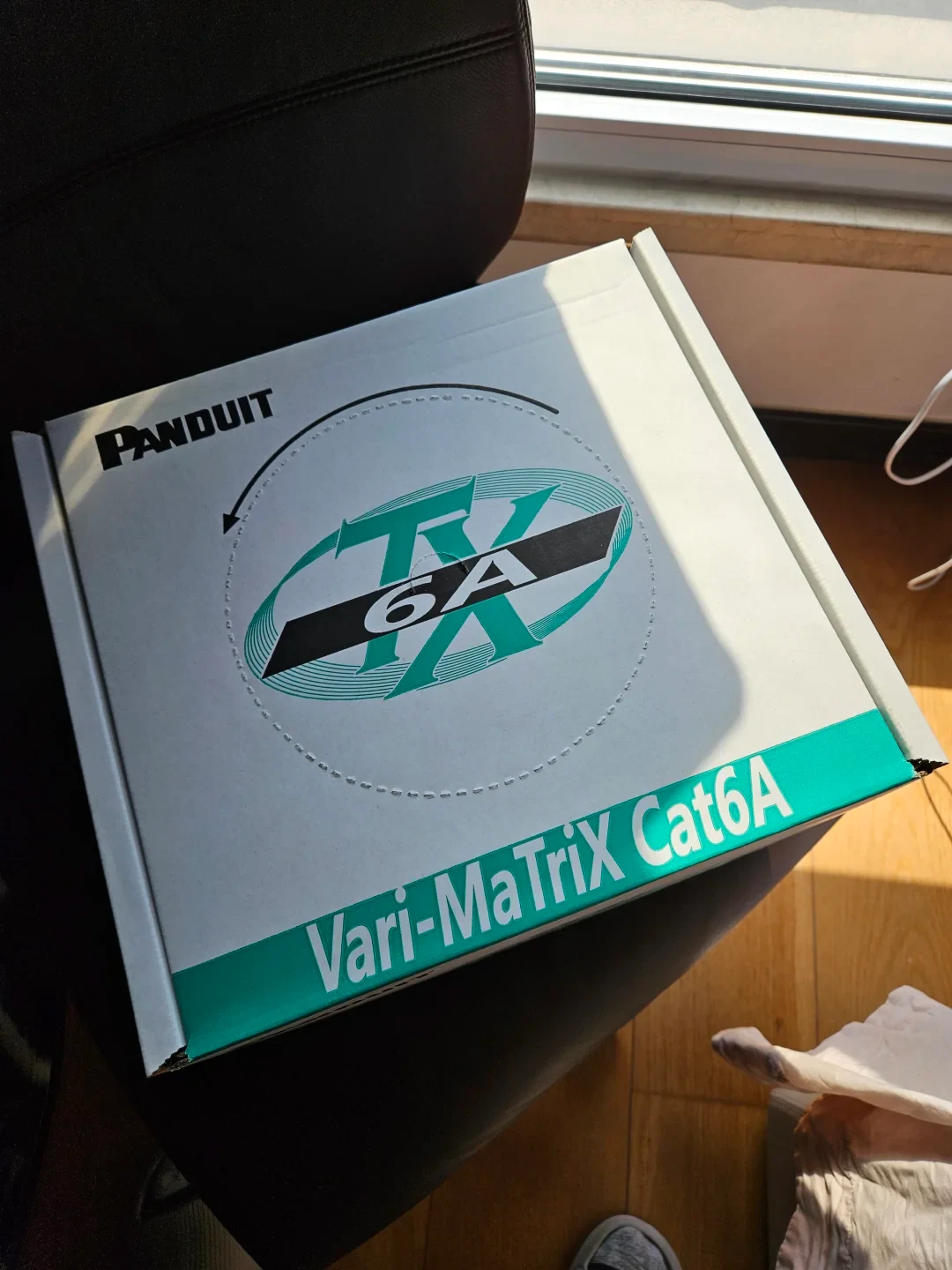 A white Panduit box labeled TX 6A and Vari-MaTriX Cat6A rests on a black chair in sunlight.