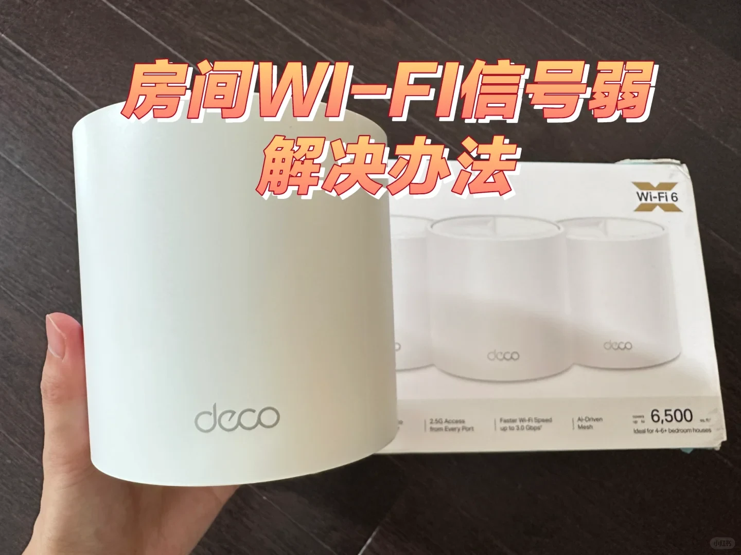 A person holds a white cylindrical Deco mesh router unit in front of its retail box, which displays three identical units and Wi-Fi 6 specifications.