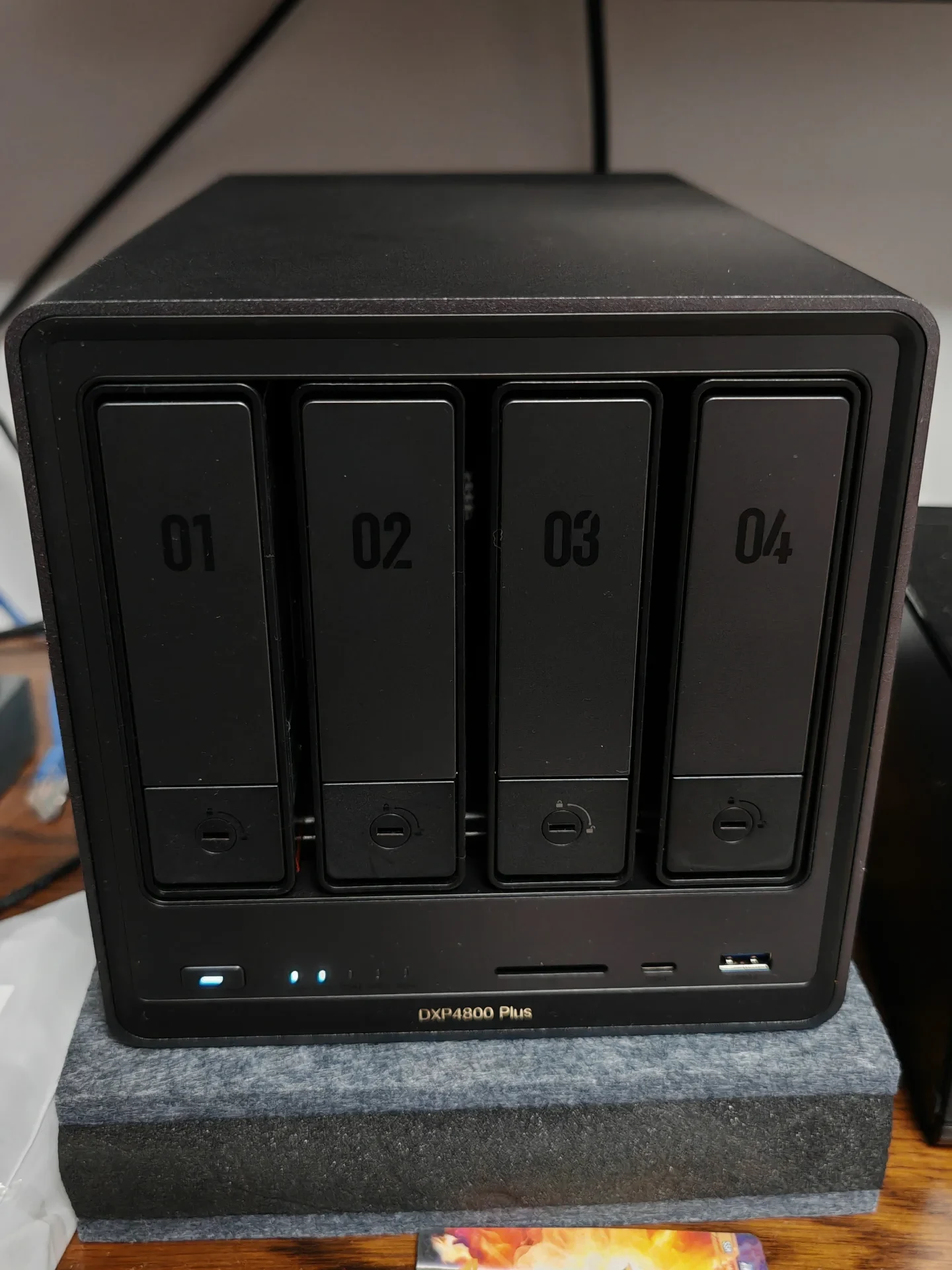 Front view of a black 4-bay DXP4800 Plus NAS device with numbered drive slots 01 through 04, status indicator lights, front ports, and the model name labeled at the bottom.