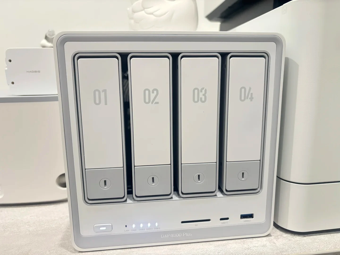 Front view of a white four-bay network-attached storage (NAS) device labeled DXP4800 Plus, with drive trays numbered 01 to 04, a power button, indicator lights, an SD card slot, and front USB ports.