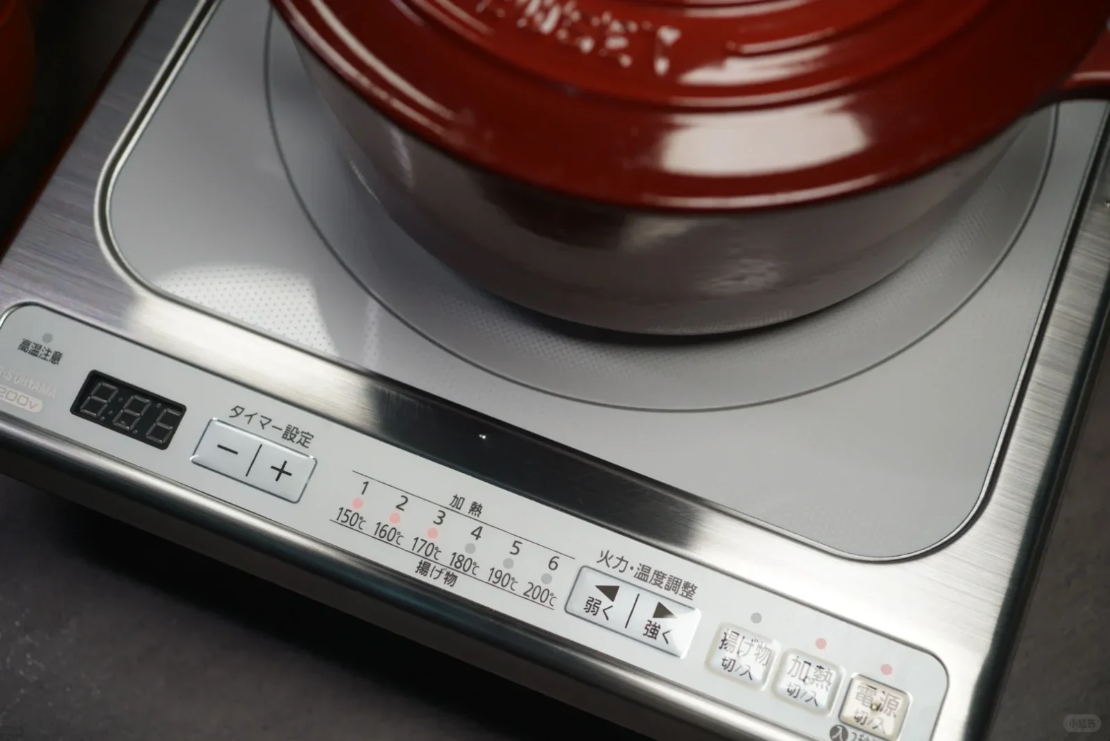 A red enameled cast-iron pot on a silver portable induction cooktop with Japanese controls.