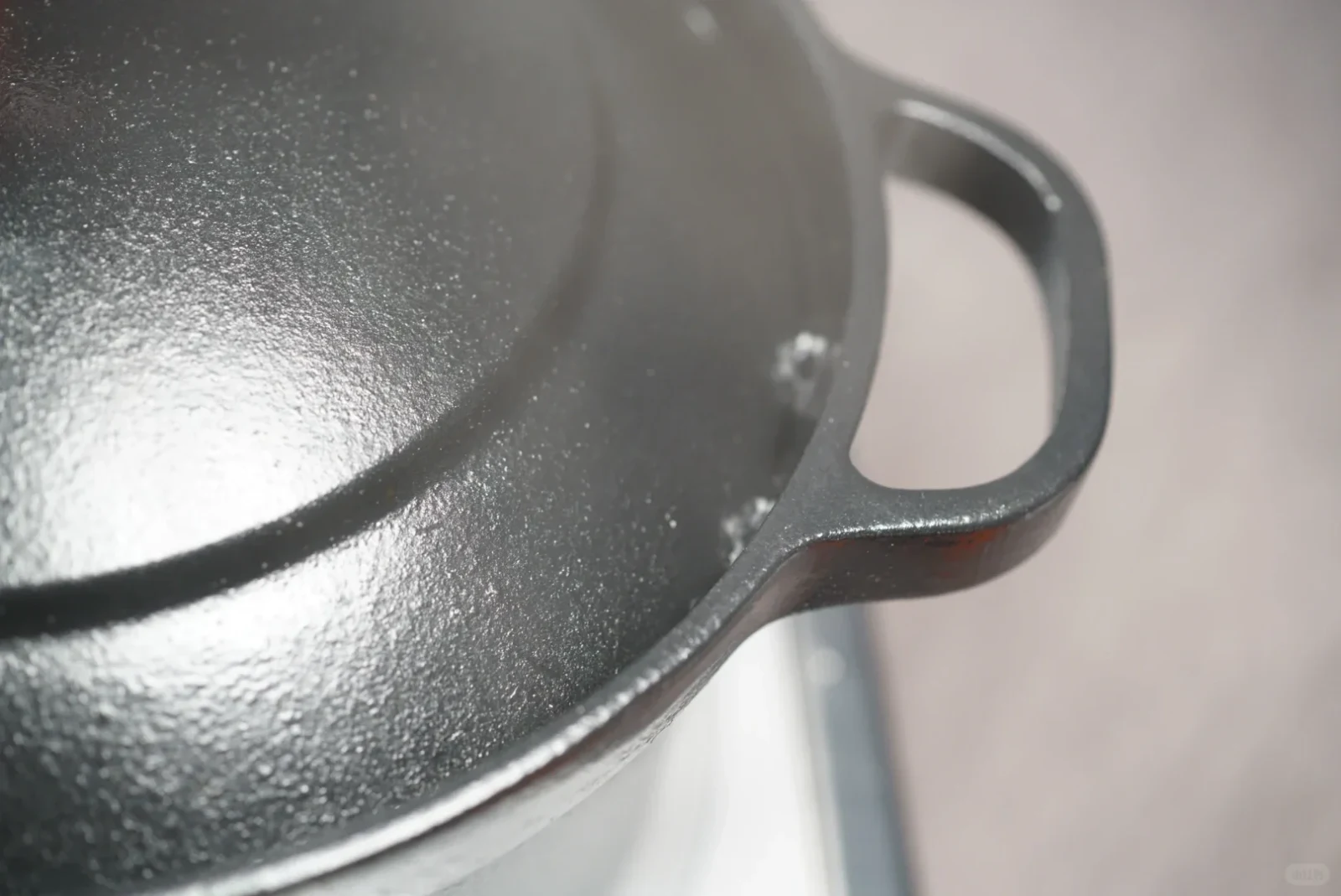 Close-up view of a black cast iron pot with its lid on, showing its textured matte finish, rim, and side handle.