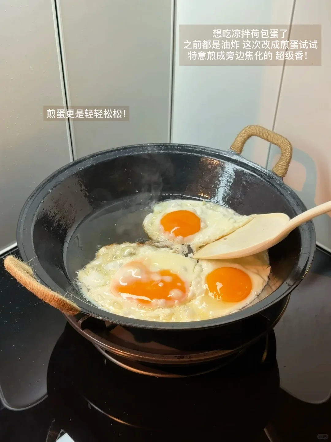 Three sunny-side-up eggs frying in oil in a black wok with twine-wrapped handles, with a spatula turning one egg.