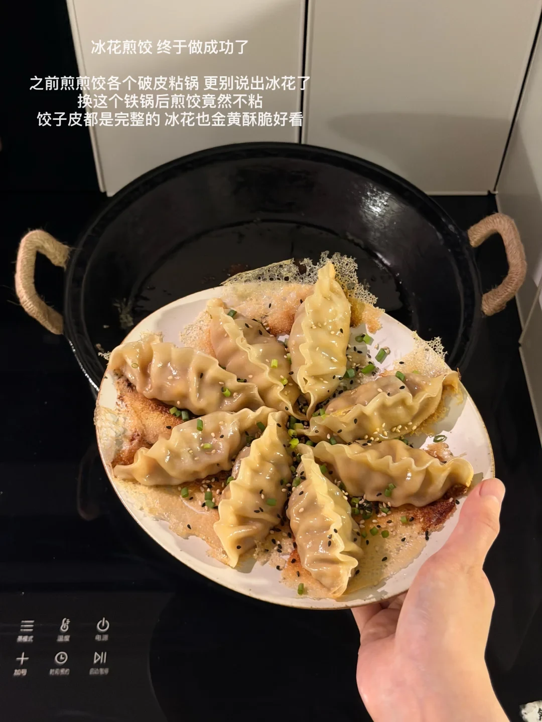 A plate of browned potstickers with a crisp lace skirt is held above a black double-handle cast-iron pan on a stovetop.