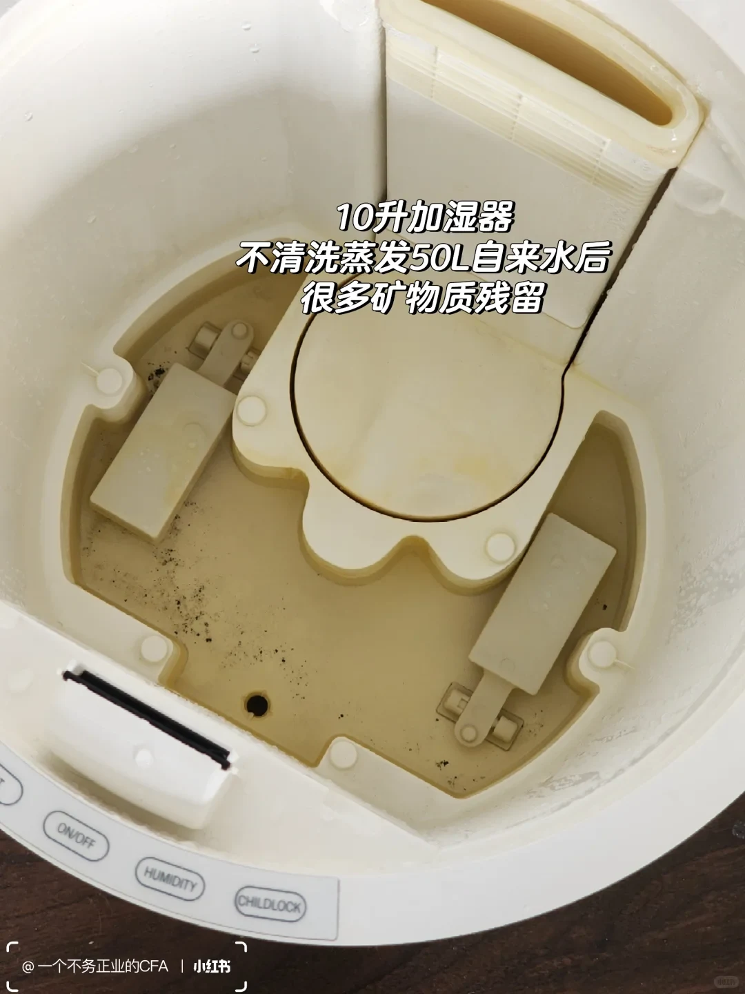 An open humidifier contains yellowish residual water with dark deposits. The owner’s overlaid caption describes mineral residue after a 10-liter humidifier evaporated 50 liters of tap water without cleaning.