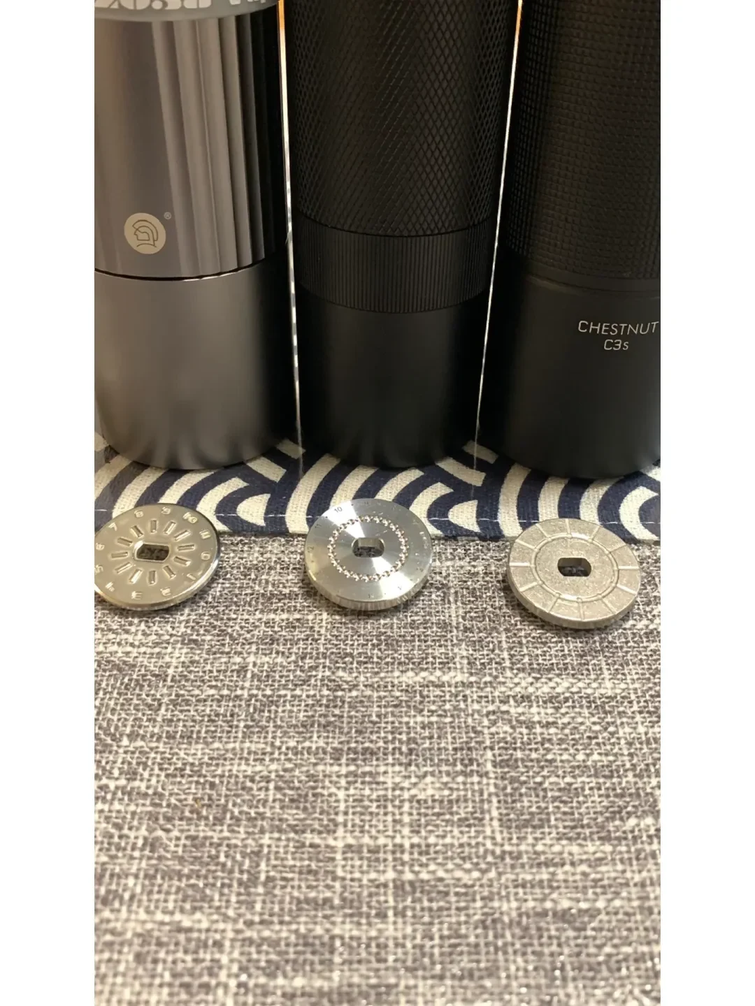 Three dark cylindrical devices stand on patterned fabric, with three separate round metal discs arranged in front of them. The right device is labeled “CHESTNUT C3s.”
