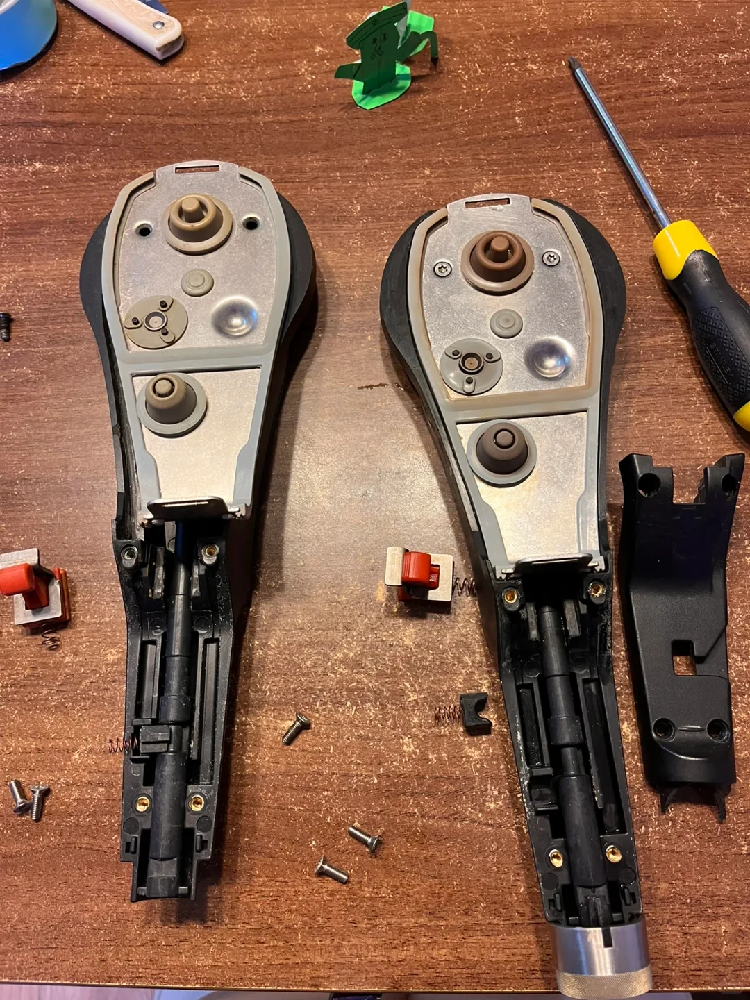 Two disassembled WMF pressure-cooker lid handles with loose screws and springs on a wooden table beside a screwdriver.