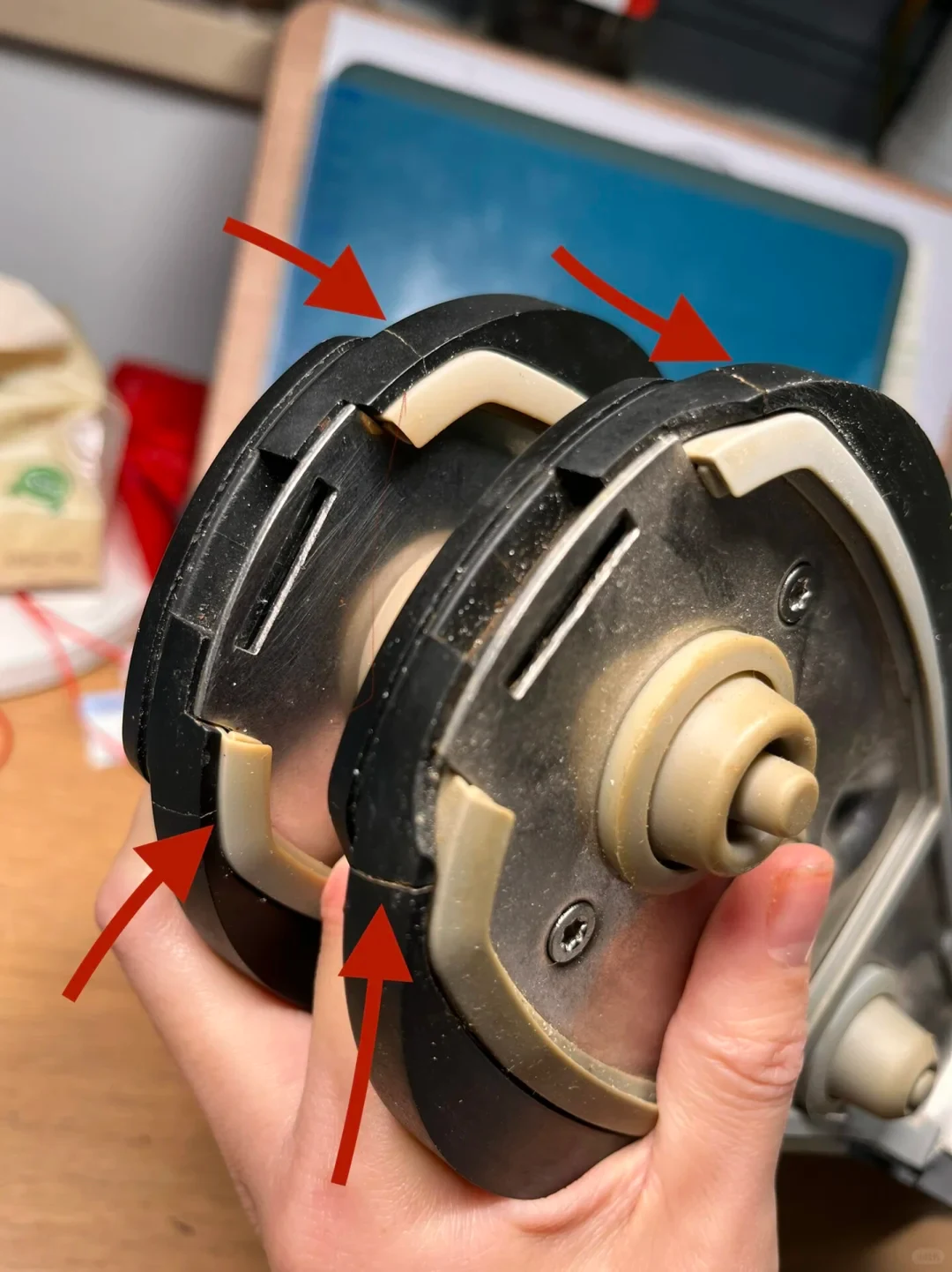 Two WMF pressure-cooker lid handles held side by side, with four red arrows pointing to cracks in their black plastic housings.