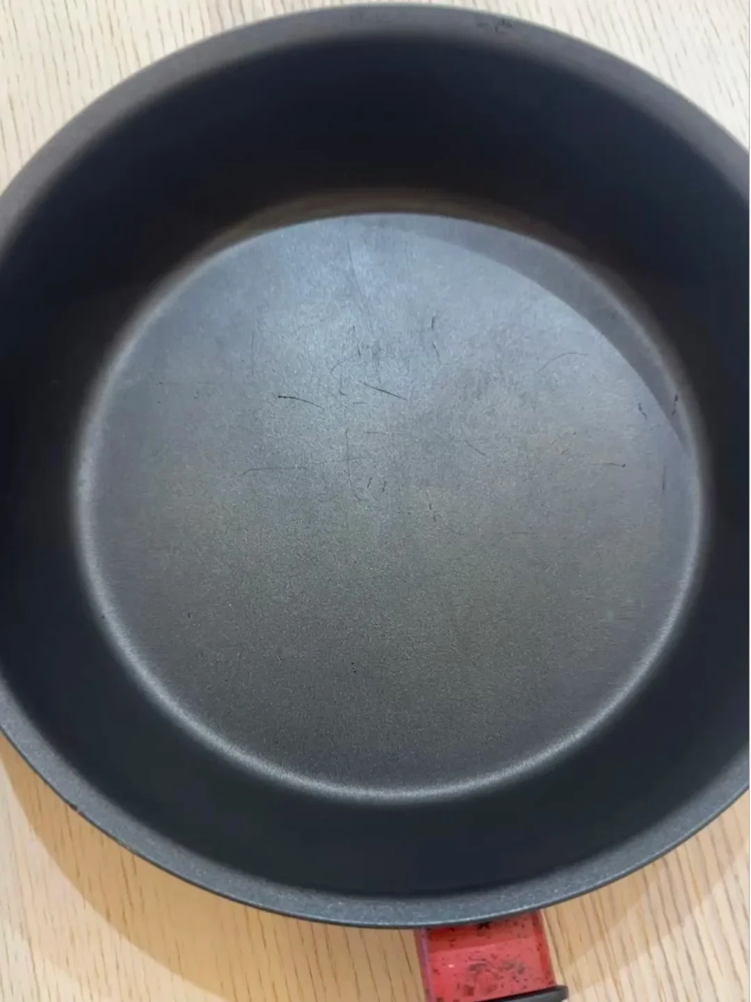 Top-down view into a black non-stick frying pan with a red handle base, showing visible surface scratches across the bottom cooking surface.