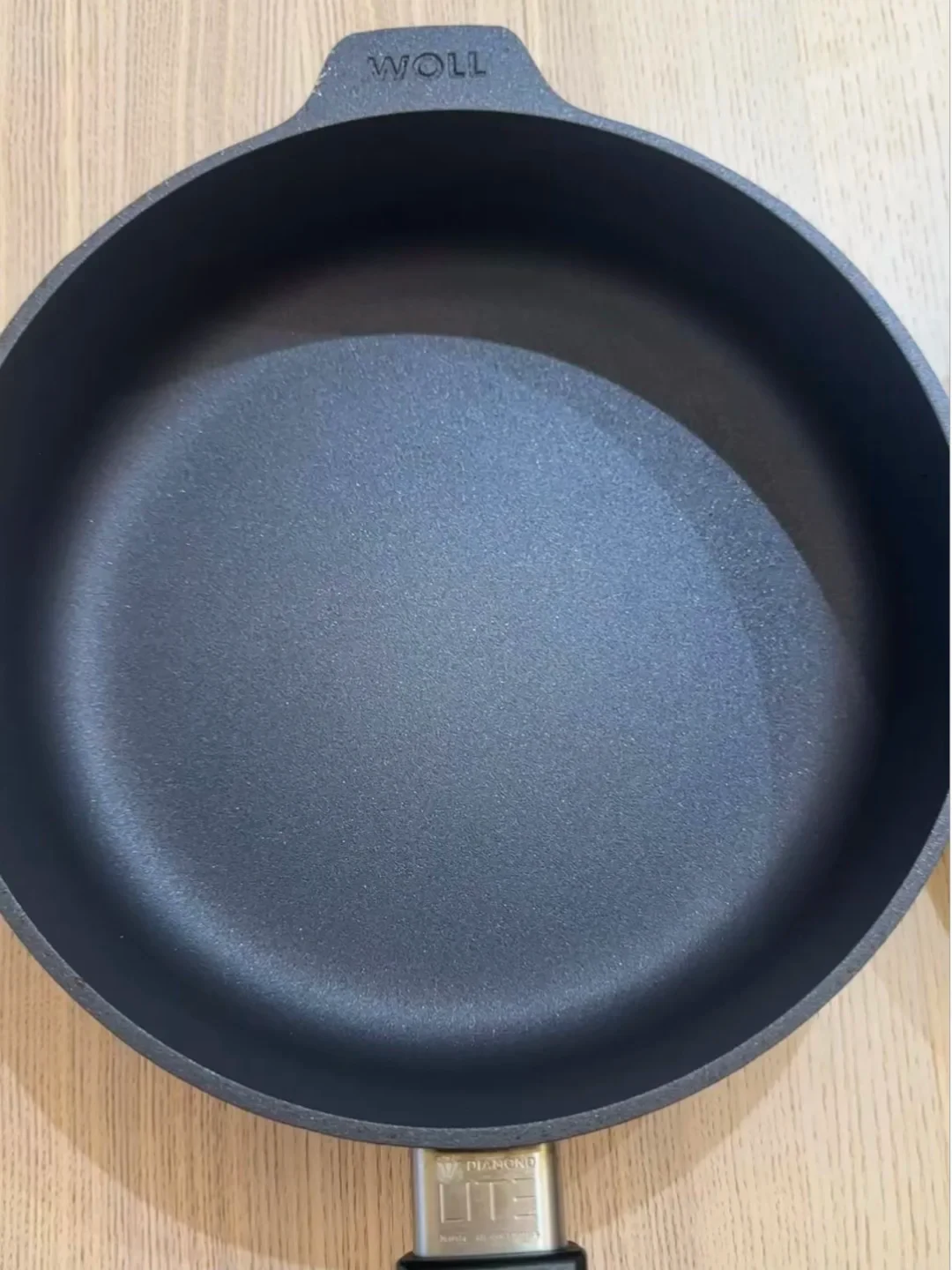 Top-down view of a black Woll Diamond Lite non-stick skillet sitting on a light wooden surface.