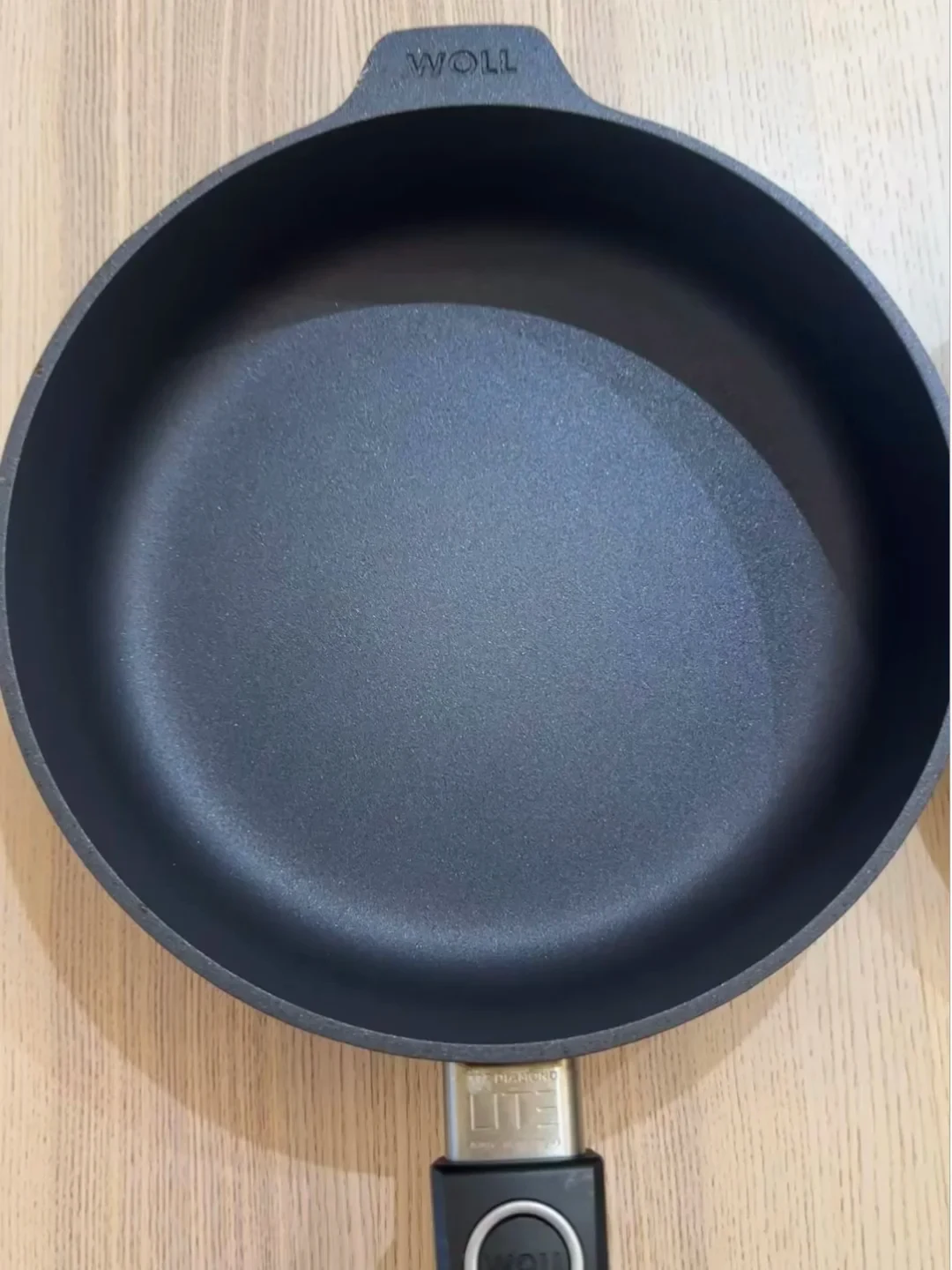 Top-down view of a Woll Diamond Lite non-stick frying pan with an intact black coated interior on a light wood surface.