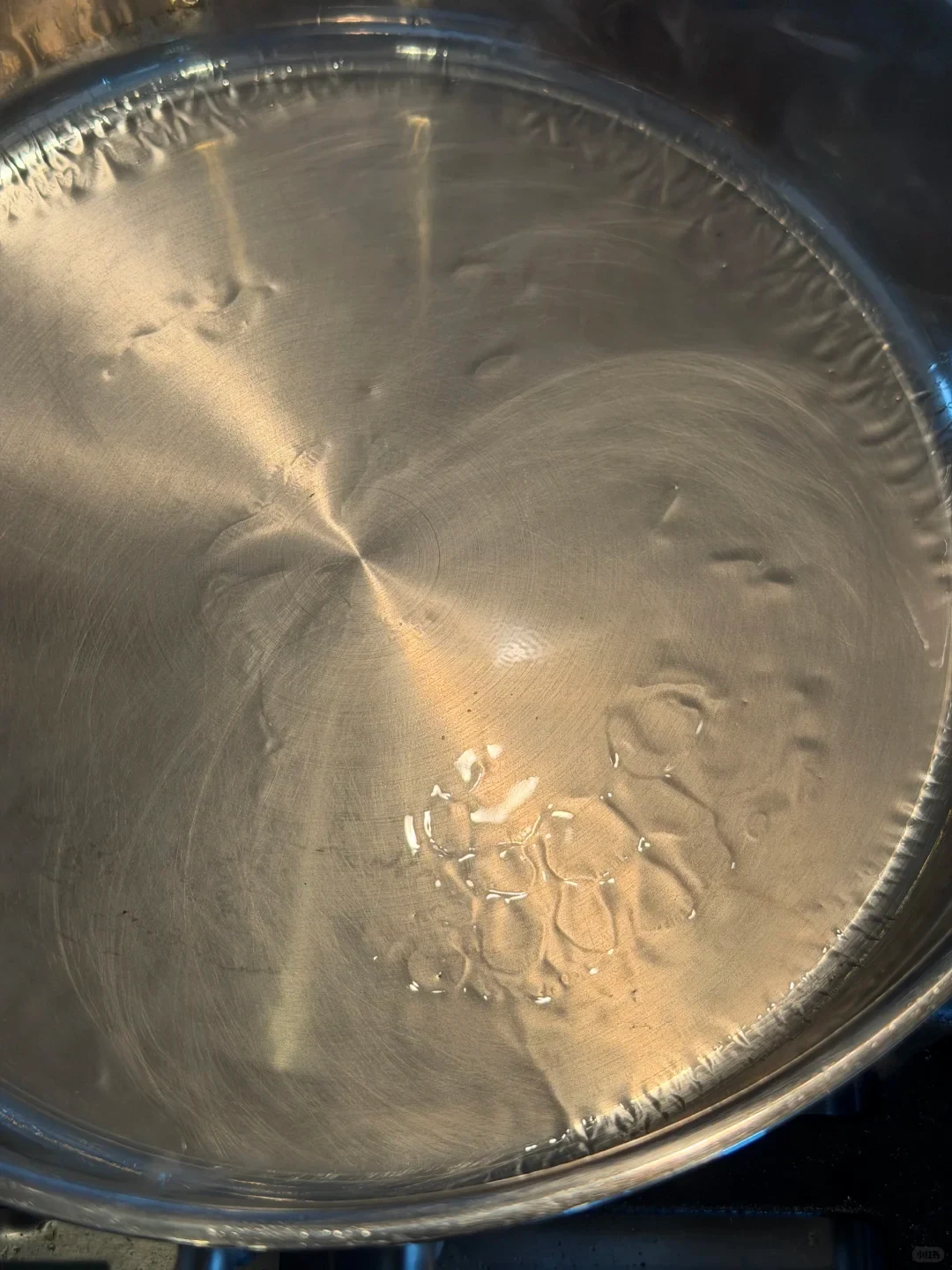 Close-up of clear droplets and reflections inside a stainless steel pan.
