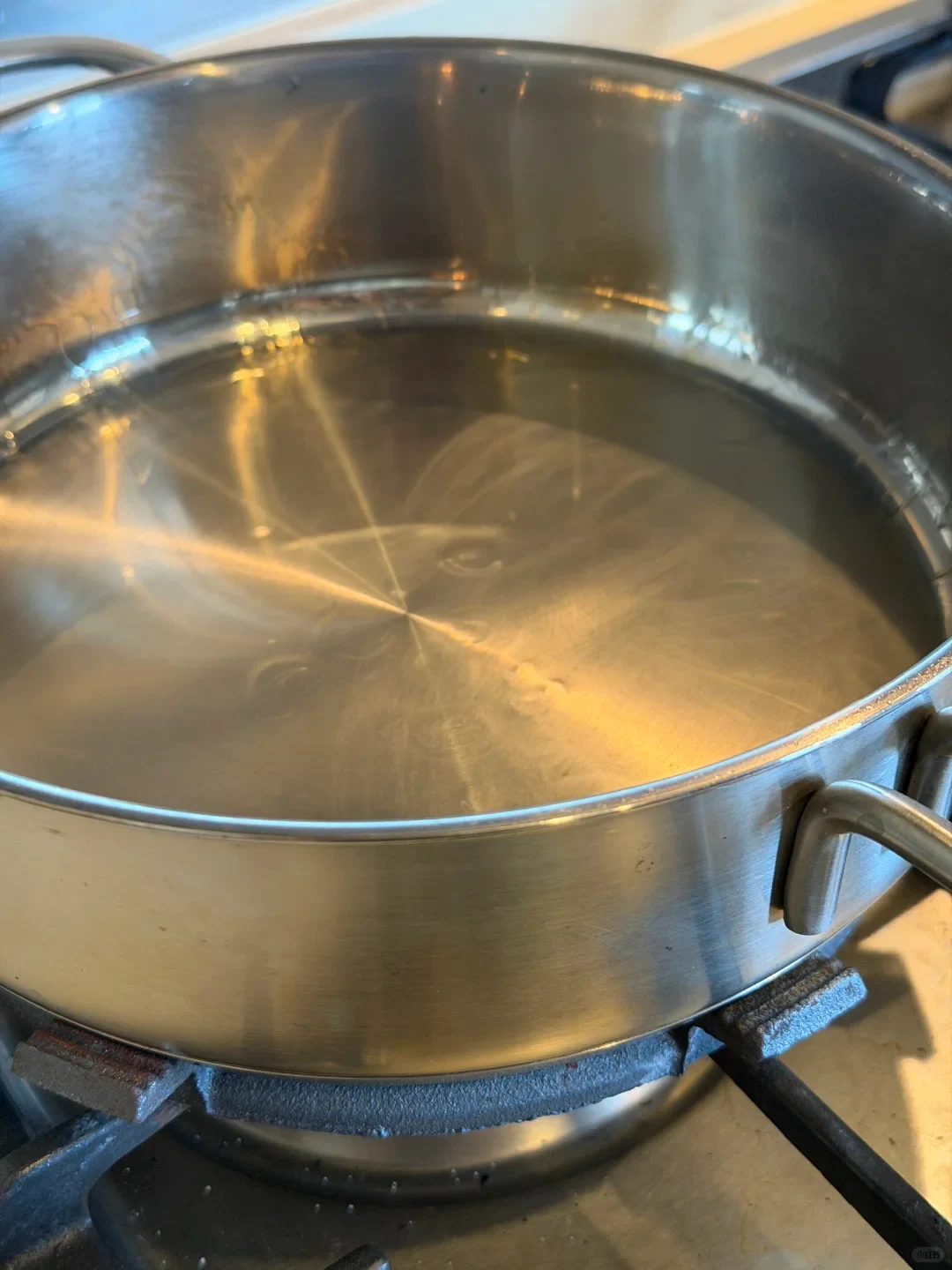 Stainless steel pan with a thin reflective layer on its base, sitting on a gas burner.