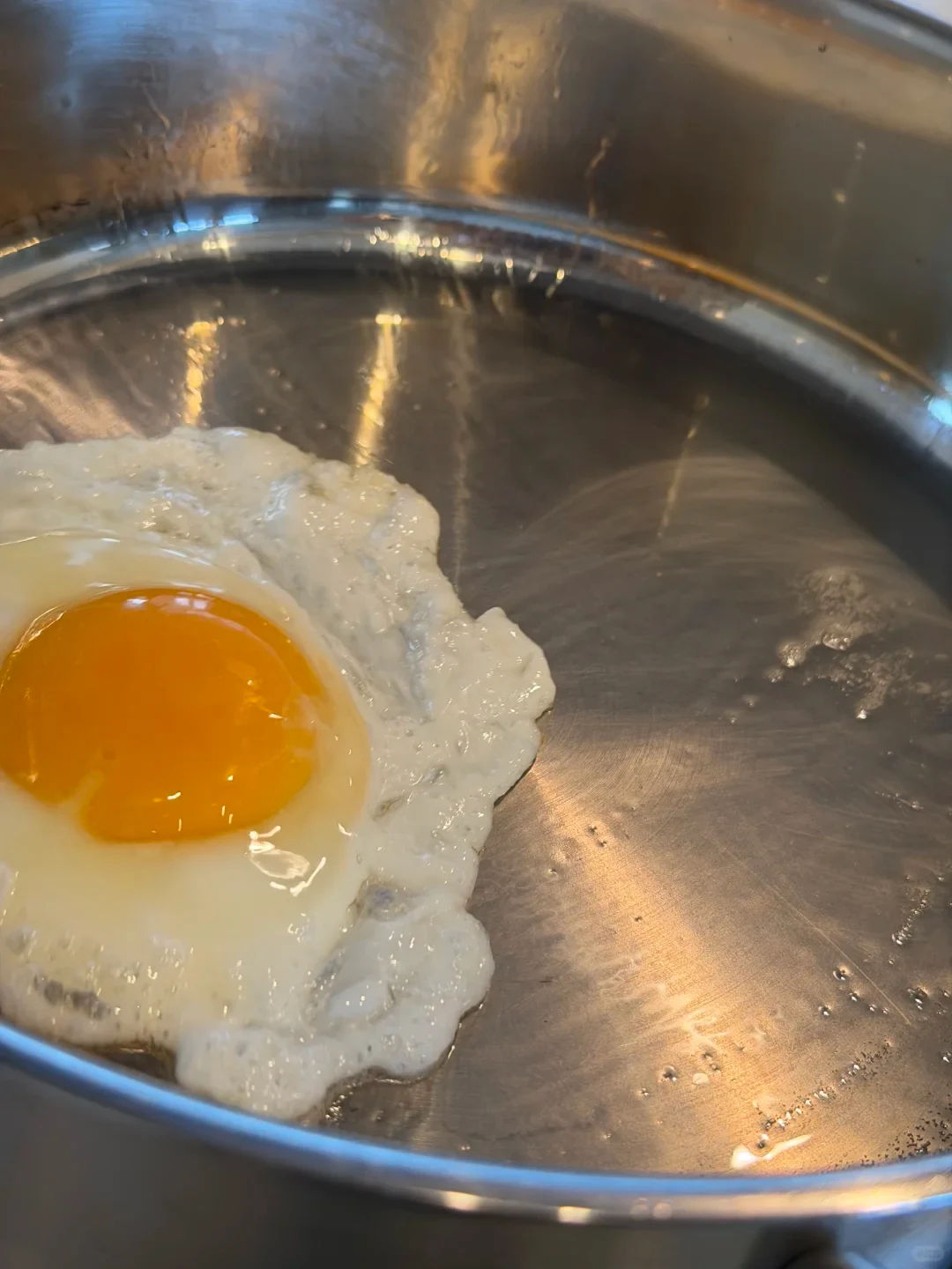 A sunny-side-up fried egg with a bright yellow yolk cooking inside a stainless steel skillet.